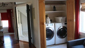 A laundry room with two washing machines, a drying rack, and a shelf with laundry supplies.
