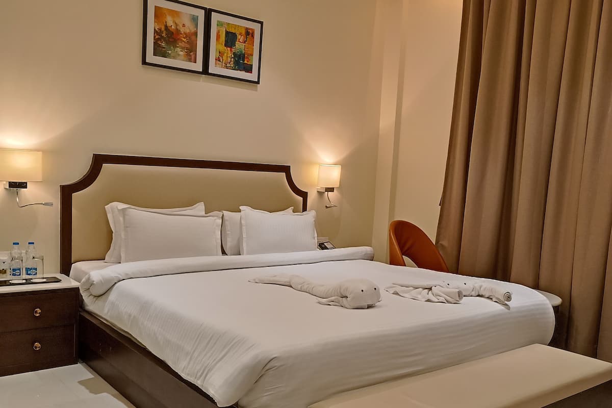 A hotel room with a large bed, bedside tables, a bench, and two wall-mounted lamps.