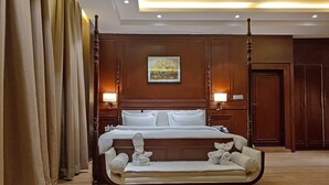 A hotel room with a large bed, a sofa, wooden paneling, and a painting on the wall. - Gulmohar Royals (Cooch Behar)