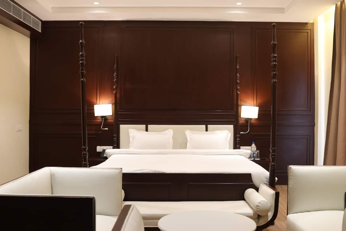 A hotel room with a large bed, two bedside tables, a round table, and two armchairs.