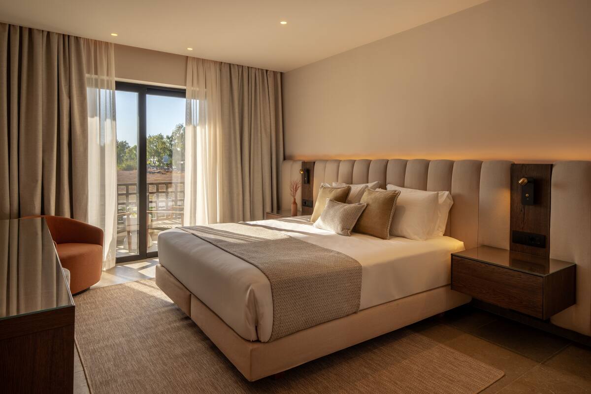 A modern bedroom with a large bed, a wooden nightstand, and a view of the outdoors through a sliding glass door.
