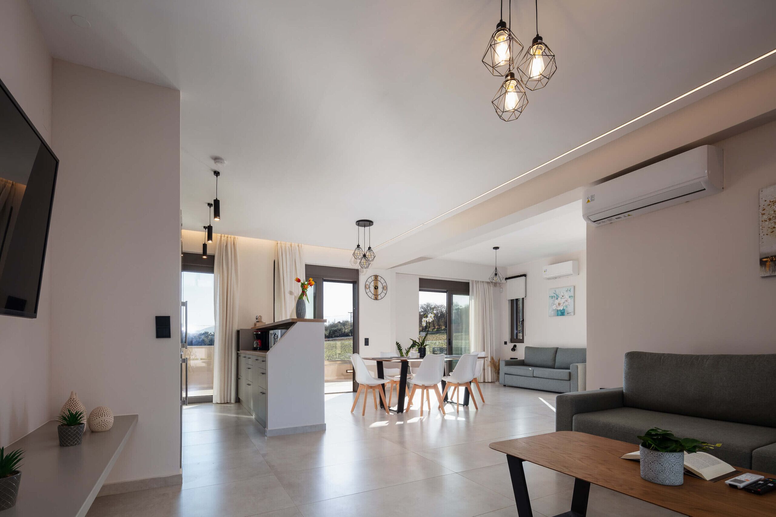 A modern living room with a sofa, a dining area with chairs, and a kitchen area with a counter.