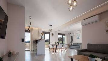 A modern living room with a sofa, a dining area with chairs, and a kitchen area with a counter.