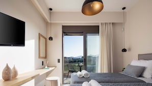 Ein modernes Hotelzimmer mit einem großen Bett, einem Fernseher, einem Schreibtisch mit Computer und einem Balkon mit Bergblick.