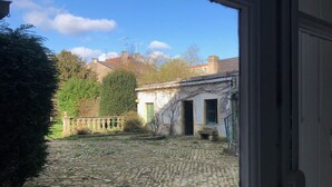 Une cour pavée de pierres, avec un mur en pierre et un bâtiment doté d’une porte verte.