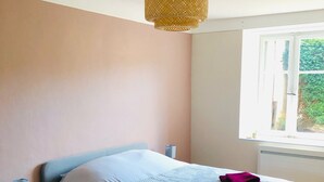 Une chambre à coucher comprenant un lit, des tables de chevet, un luminaire suspendu et une fenêtre donnant sur un paysage verdoyant.