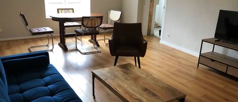 A living room with a blue sofa, a wooden coffee table, a TV stand, and a dining area with chairs and a table.