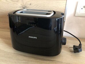 Een zwarte Philips toaster op een houten oppervlak, met een snoer in het stopcontact.
