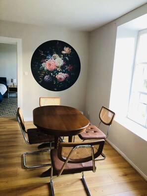 Een eetruimte met een ronde houten tafel, vier stoelen en een groot bloemschilderij aan de muur.