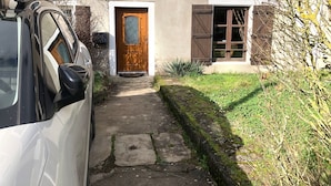 Un bâtiment doté d’une porte centrale, d’une porte latérale et d’une fenêtre avec des volets. Une voiture est garée devant.