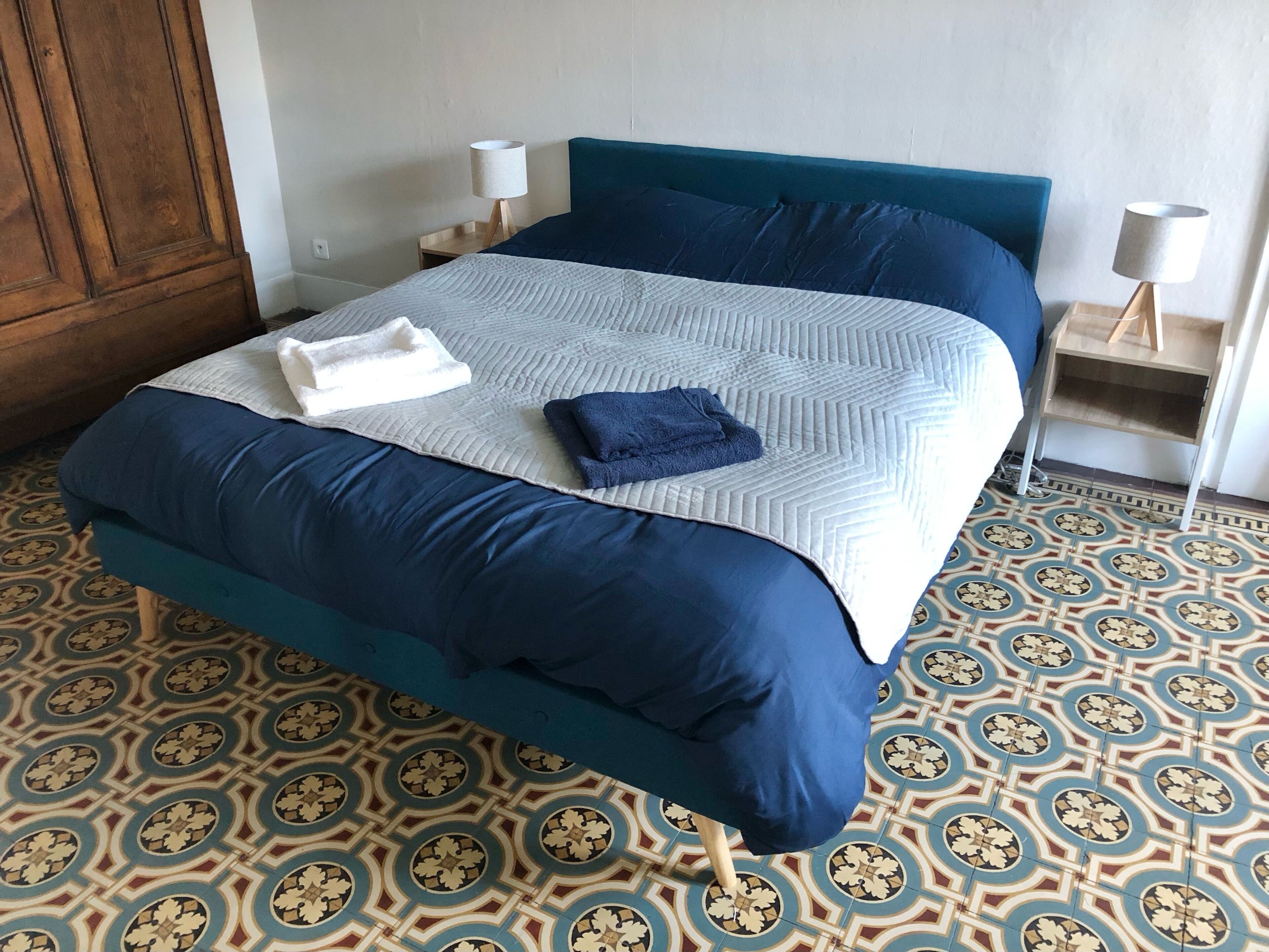 Ein ordentlich gemachtes Bett mit blauem Kopfteil und einem gemusterten Boden.