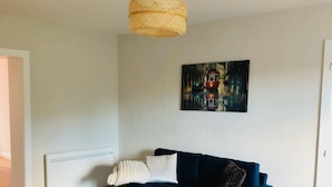 Un salon moderne avec un canapé bleu, un fauteuil marron, une table basse en bois et un luminaire suspendu en fibres tressées.