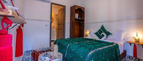 Ein gemütliches Schlafzimmer mit einem Bett, einem Holzschrank, einem kleinen Tisch mit Dekoration und einem an der Wand befestigten Regal mit einer Lampe.