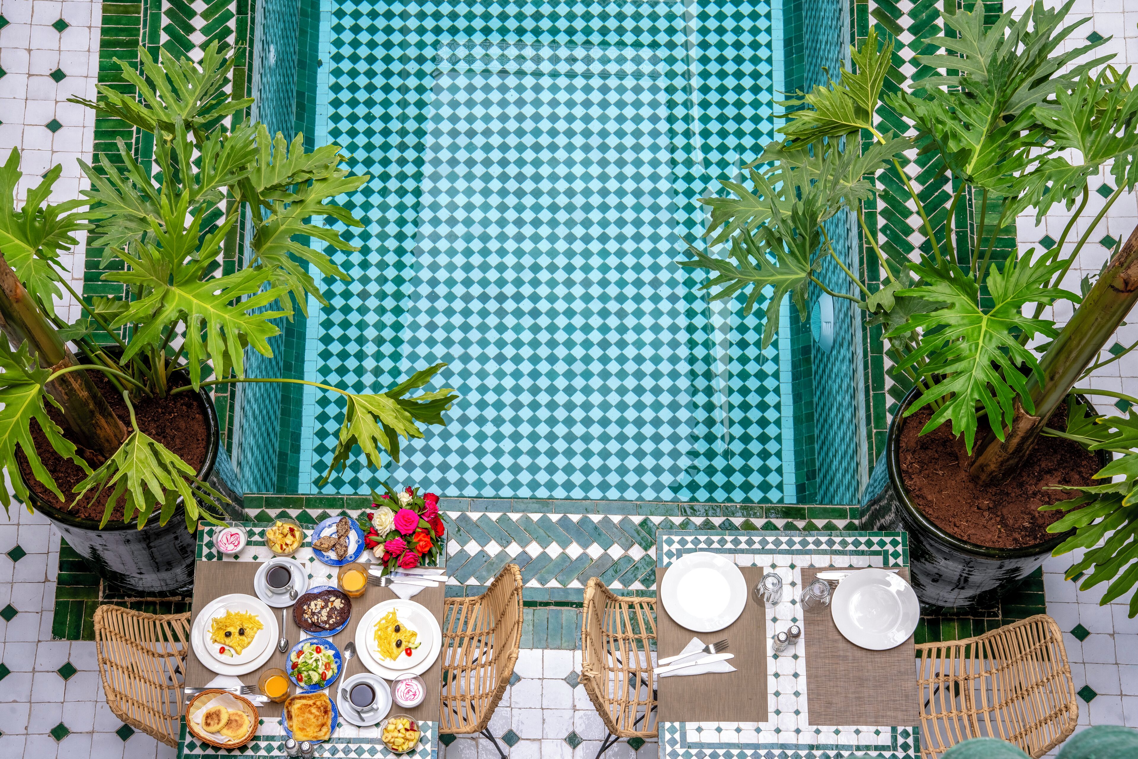 A dining area with a table set for two, surrounded by potted plants and a tiled floor.