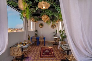 Un comedor con suelo a cuadros, muebles de mimbre y plantas colgantes.