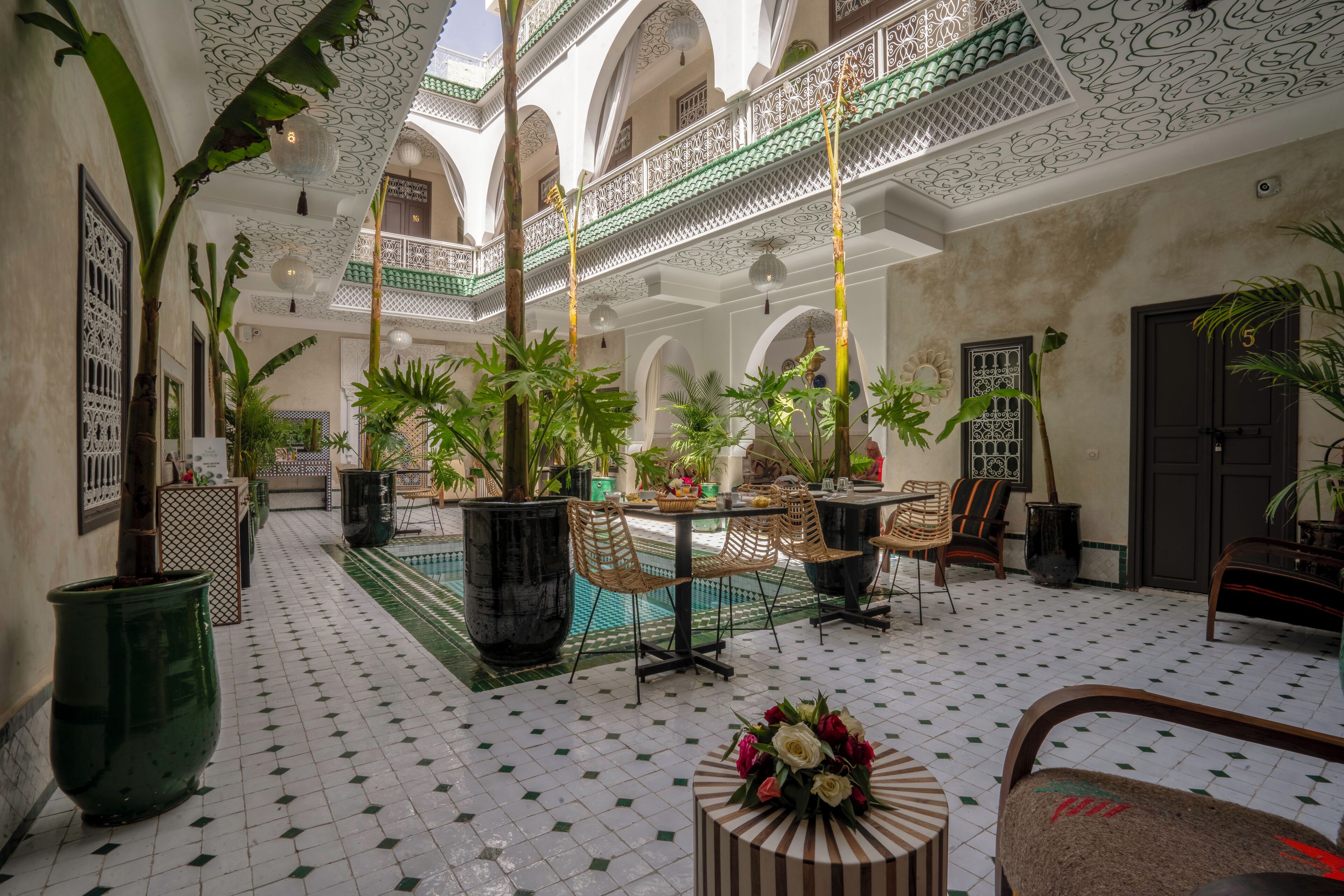 A courtyard with tiled flooring, potted plants, outdoor seating, and a decorative ceiling.