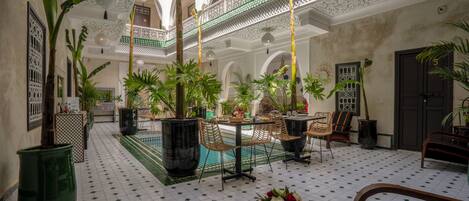 A courtyard with tiled flooring, potted plants, outdoor seating, and a decorative ceiling.