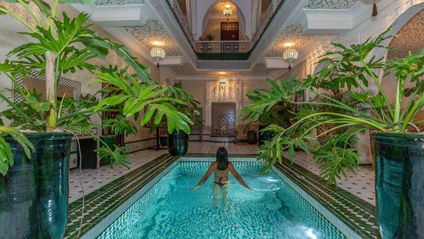 Una piscina interior con una persona nadando, rodeada de grandes macetas y detalles arquitectónicos ornamentales.