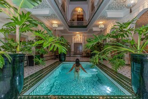 Una piscina interior con una persona nadando, rodeada de grandes macetas y detalles arquitectónicos ornamentales.