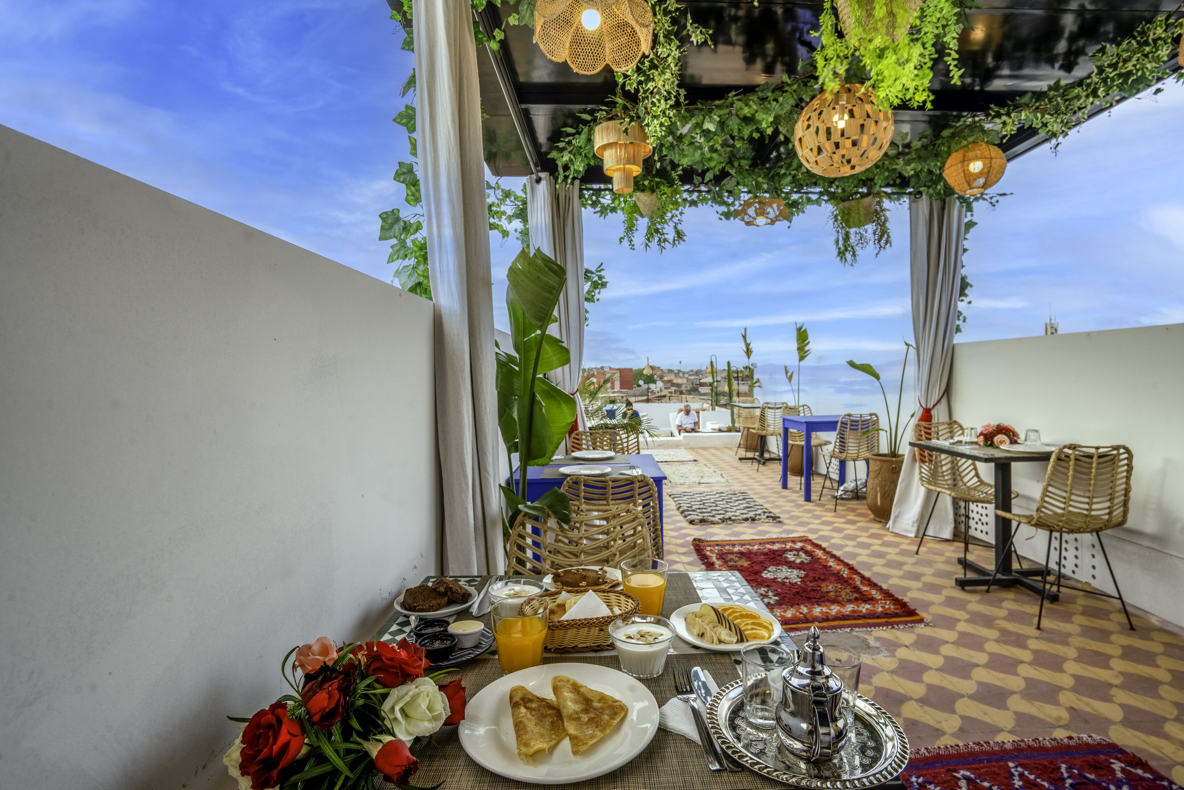 A breakfast setting with a table set for two, featuring plates of food, a basket of bread, and a vase of flowers.