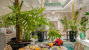 Desayuno servido en una mesa para dos, con diversos platos, bebidas y una planta en maceta.