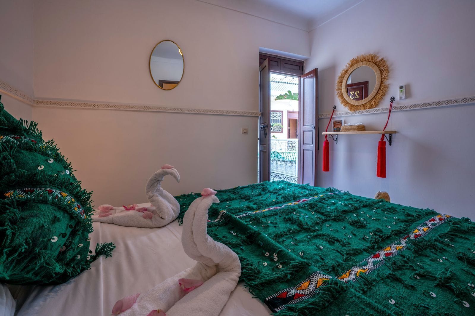 Una habitación con una cama cubierta con mantas verdes, un espejo en la pared y una puerta que da al exterior.