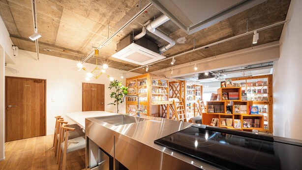 A modern kitchen with a stainless steel island, wooden stools, and a built-in bookshelf filled with books. - MANGA ART HOTEL BAKUROCHO (Tokyo)