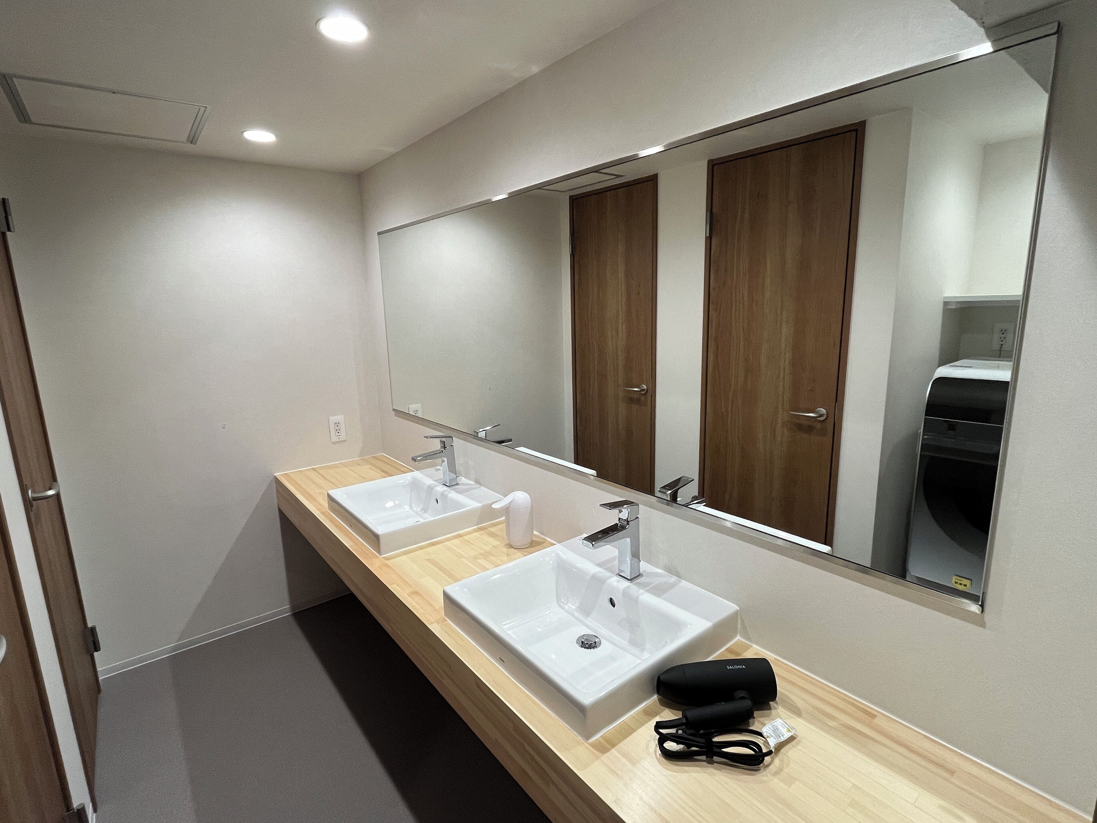 Une salle de bain moderne avec deux vasques, un grand miroir, un meuble-lavabo en bois et un sèche-cheveux posé sur le comptoir.