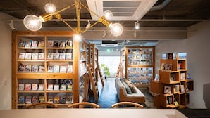 A bookstore with wooden shelves filled with manga and books, a central aisle with a bench, and a modern chandelier. - MANGA ART HOTEL BAKUROCHO (Tokyo)