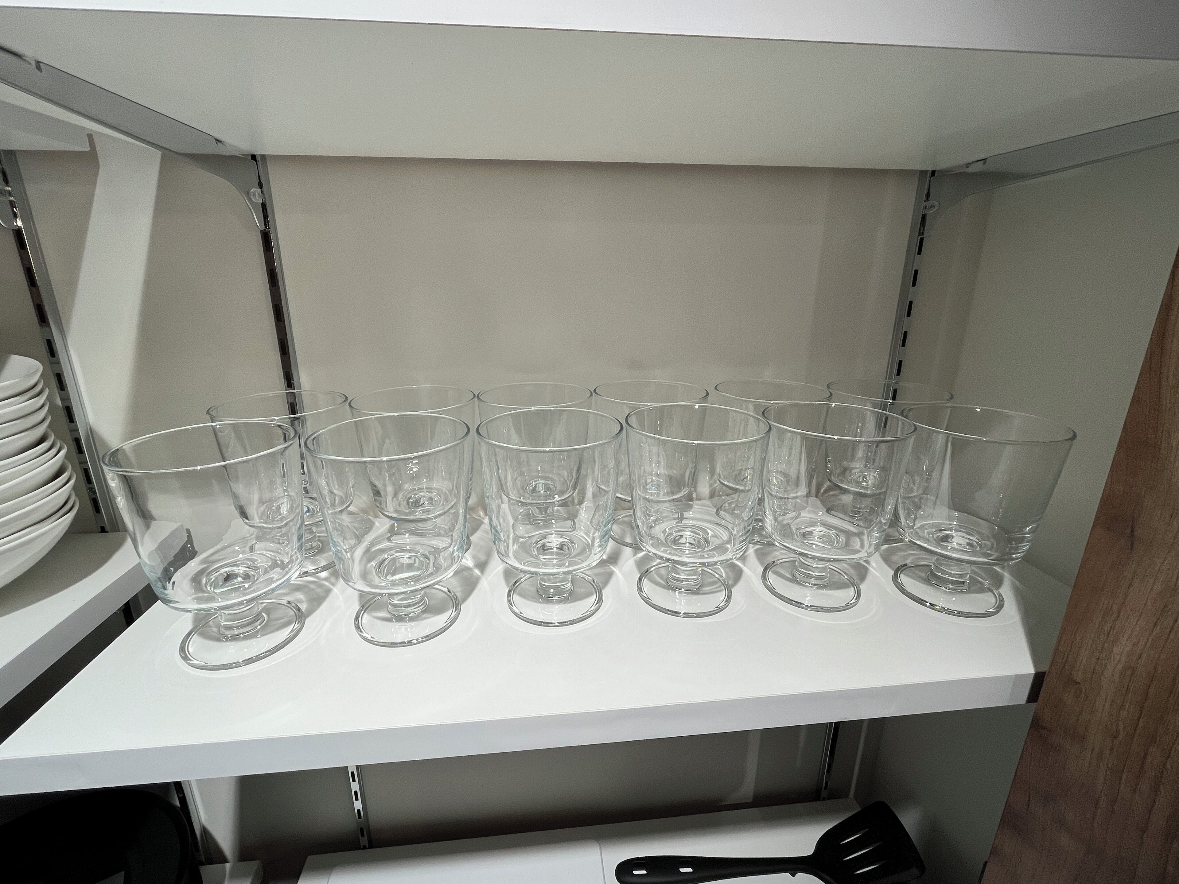 A kitchen shelf with multiple clear glass tumblers and a black spatula.