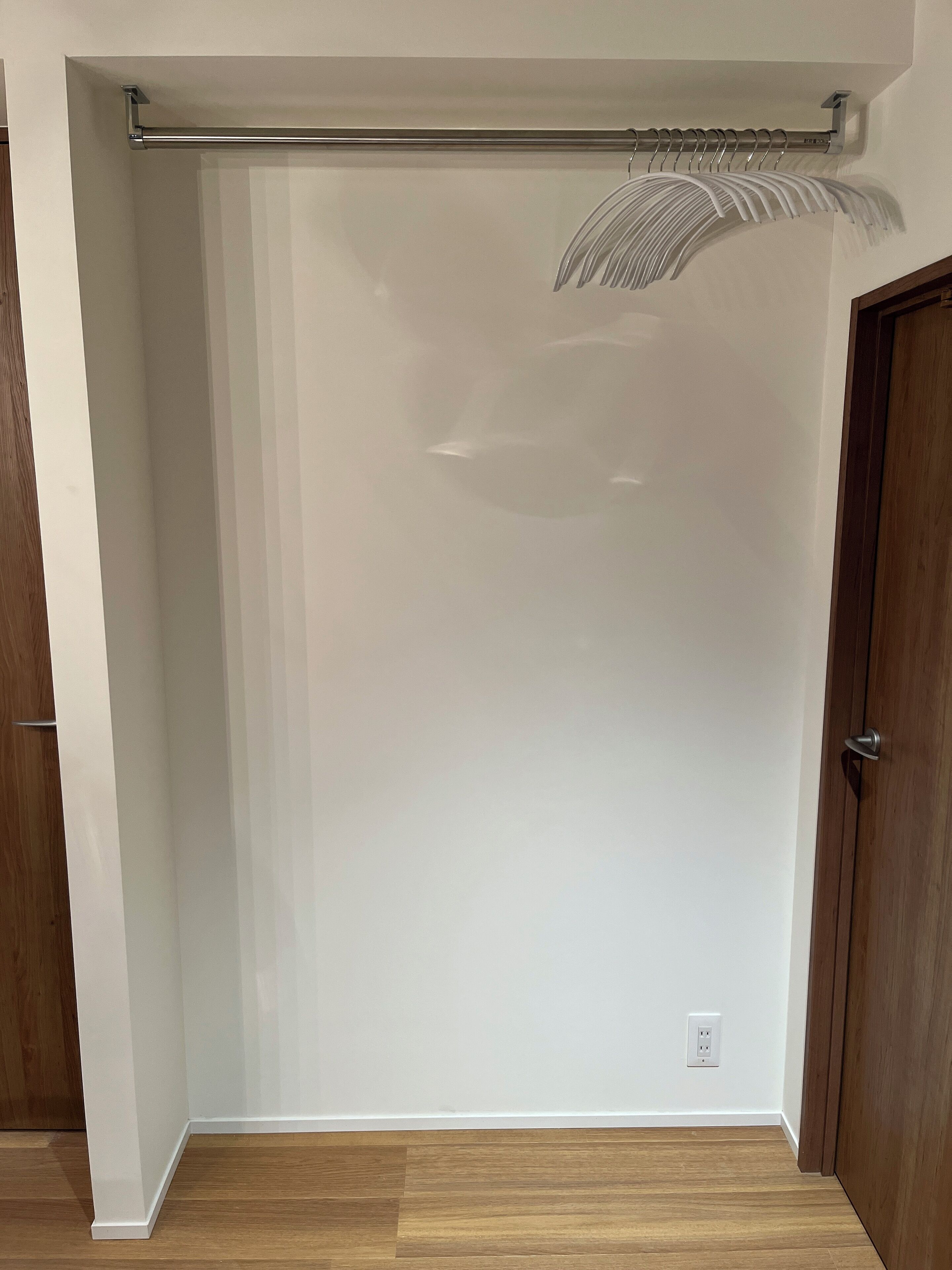 A room with a wooden floor, white walls, a door, and a ceiling-mounted towel rack.