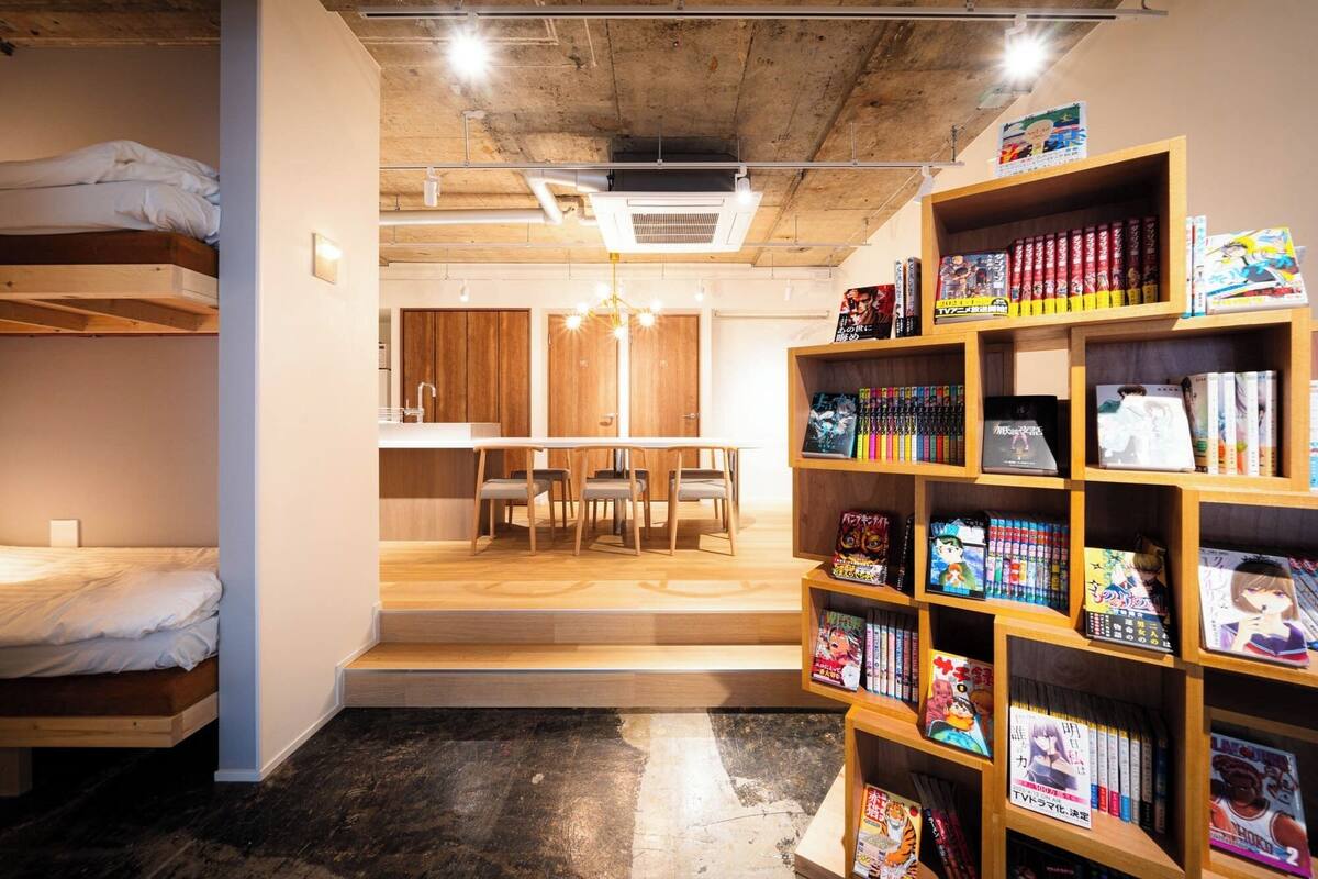 A room with bunk beds, a dining area, and a bookshelf filled with manga.