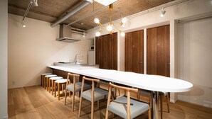 A modern kitchen with a long white countertop, wooden chairs, and a built-in oven. - MANGA ART HOTEL BAKUROCHO (Tokyo)