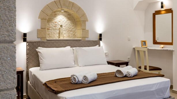 A hotel room with a bed, a stone arch, a nightstand, a chair, and a mirror. - The Owl House - Studio #2 (Chania)