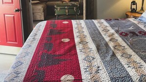 Une pièce avec un lit, une porte rouge, une peau d’animal accrochée au mur, une valise verte et une lampe.
