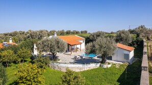 Une villa avec un toit recouvert de tuiles rouges, une piscine et un mur de pierre qui entoure la propriété.
