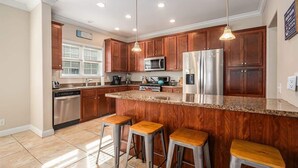A modern kitchen with wooden cabinets, stainless steel appliances, a granite countertop, and three bar stools. - Hounds on Hazel (South Haven)