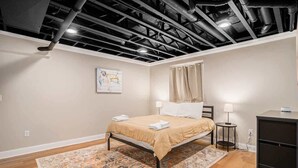 A bedroom with a bed, a nightstand, a lamp, a desk, and a ceiling with exposed ductwork. - Hounds on Hazel (South Haven)