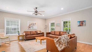 A spacious living room with two brown leather sofas, a wooden coffee table, and a ceiling fan. - Hounds on Hazel (South Haven)