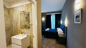 Et moderne hotelværelse med et marmorbadeværelse, en seng med lyseblåt sengegavl og et billede på væggen.