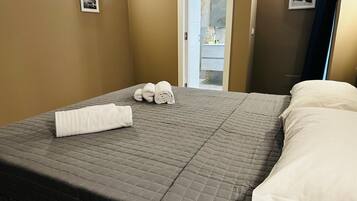 A neatly made bed with a quilted gray bedspread, two rolled white towels, and a white pillow.