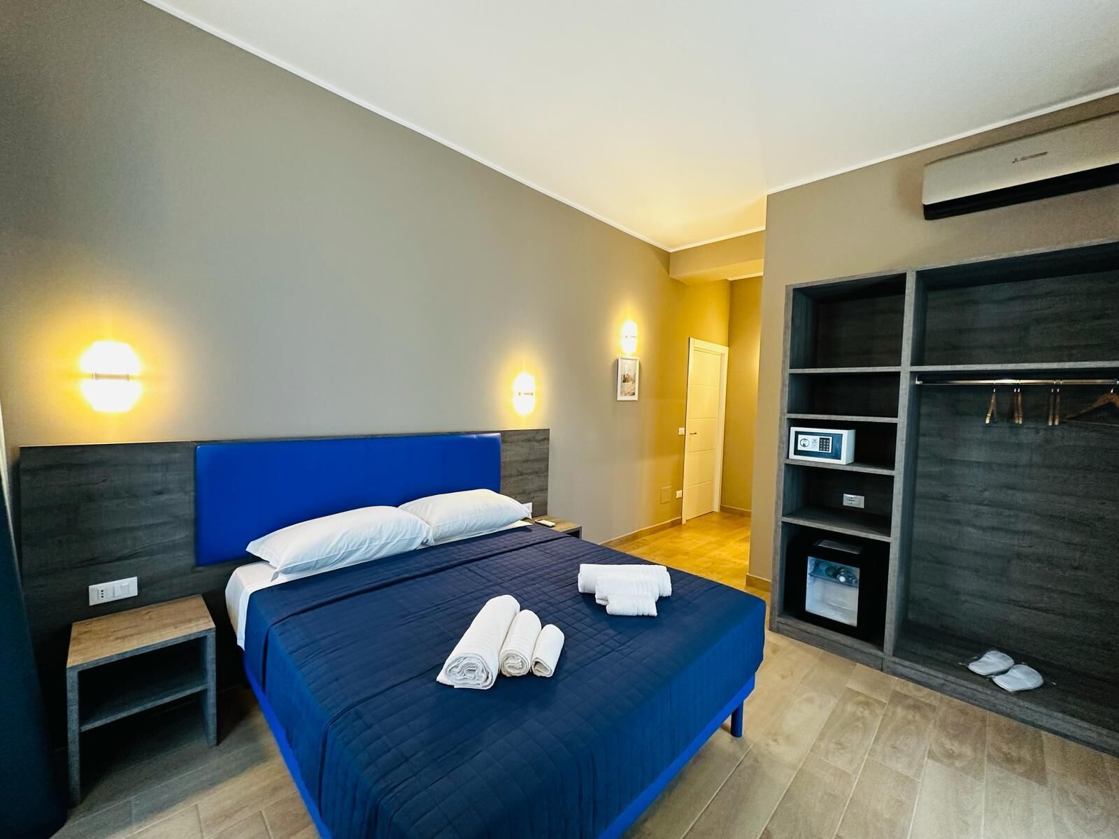 A modern hotel room with a large bed, bedside tables, a wardrobe, and a digital control panel.