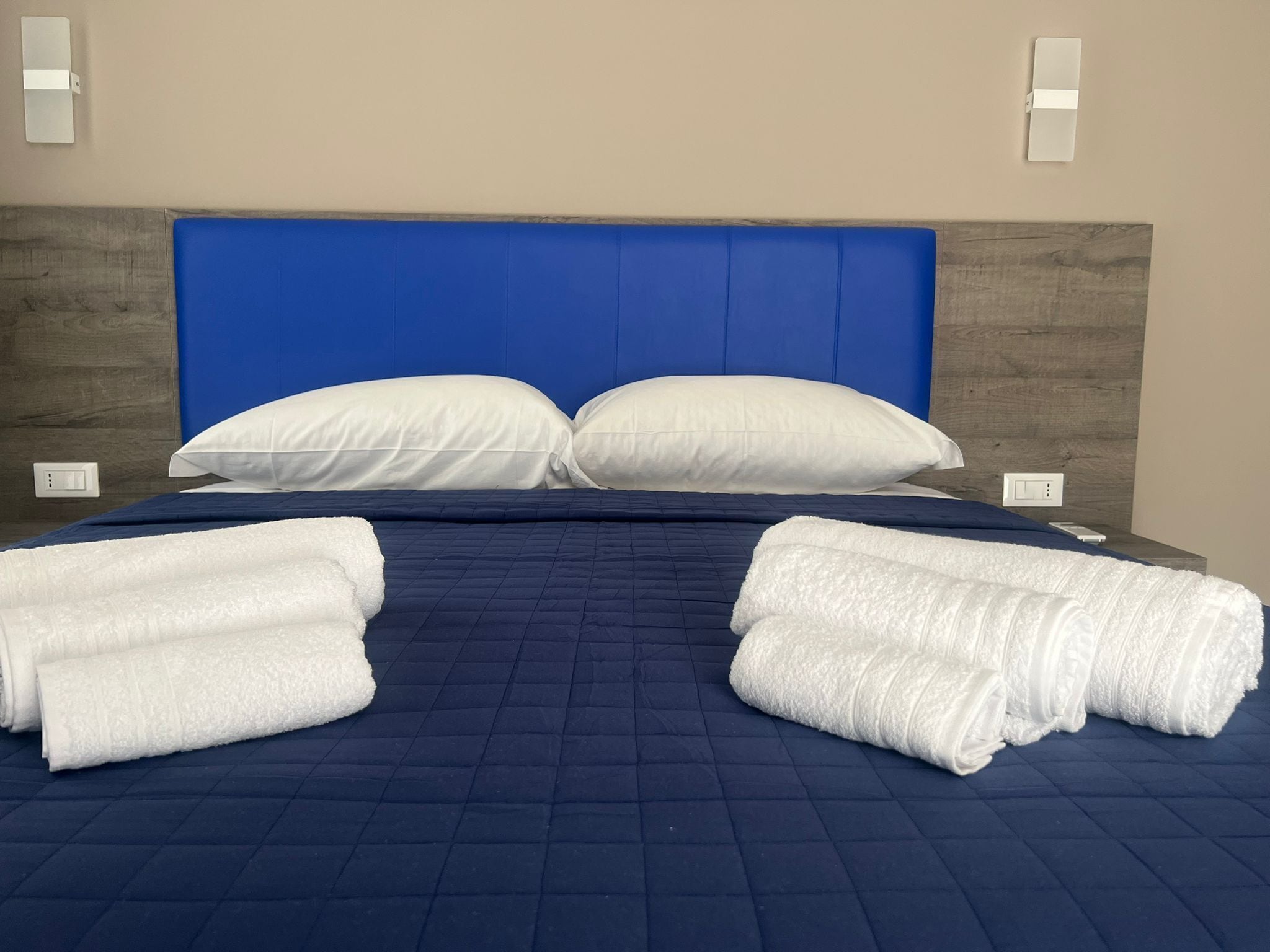 A neatly made bed with a blue headboard, white pillows, and rolled white towels.