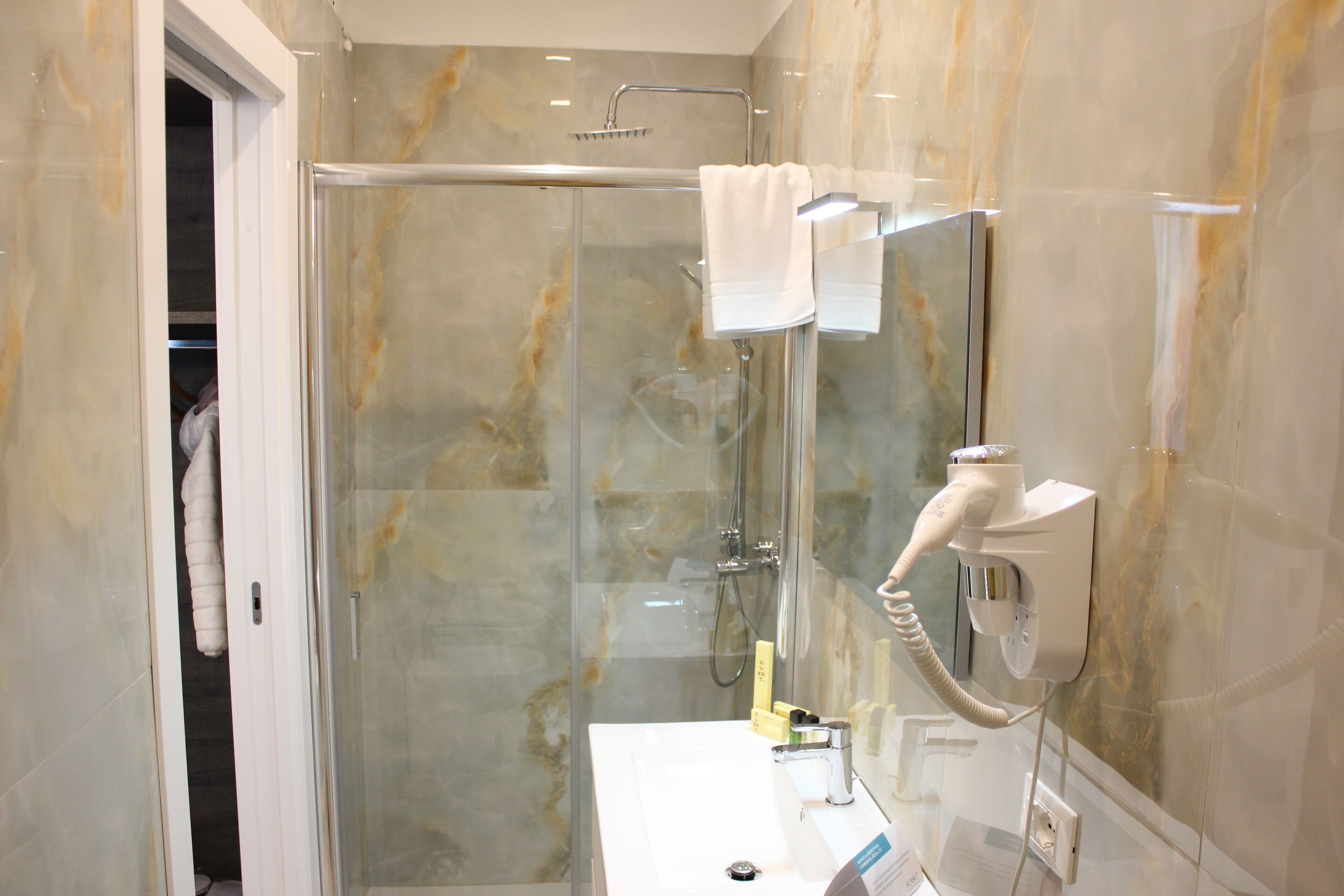 Een moderne badkamer met een douchecabine van glas, een witte wastafel en een handdoek aan een rek.