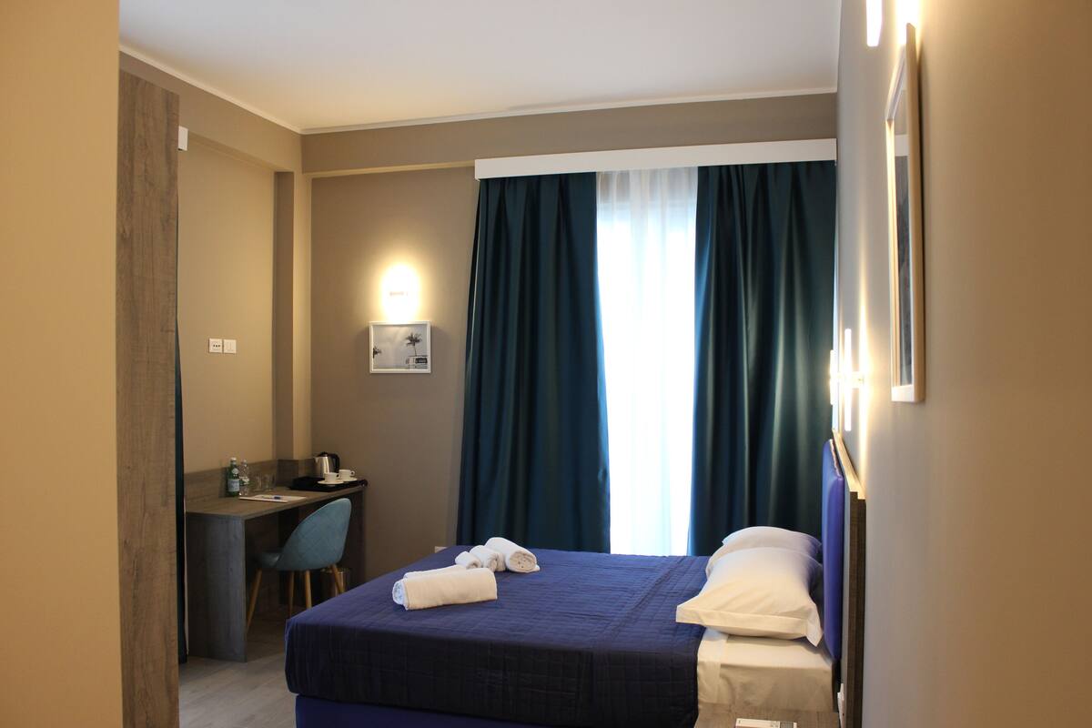 A hotel room with a bed, a desk, a chair, and a window with curtains.