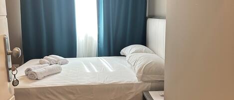 Una habitación de hotel con una cama, una mesita de noche, un cuadro en la pared y una ventana con cortinas.