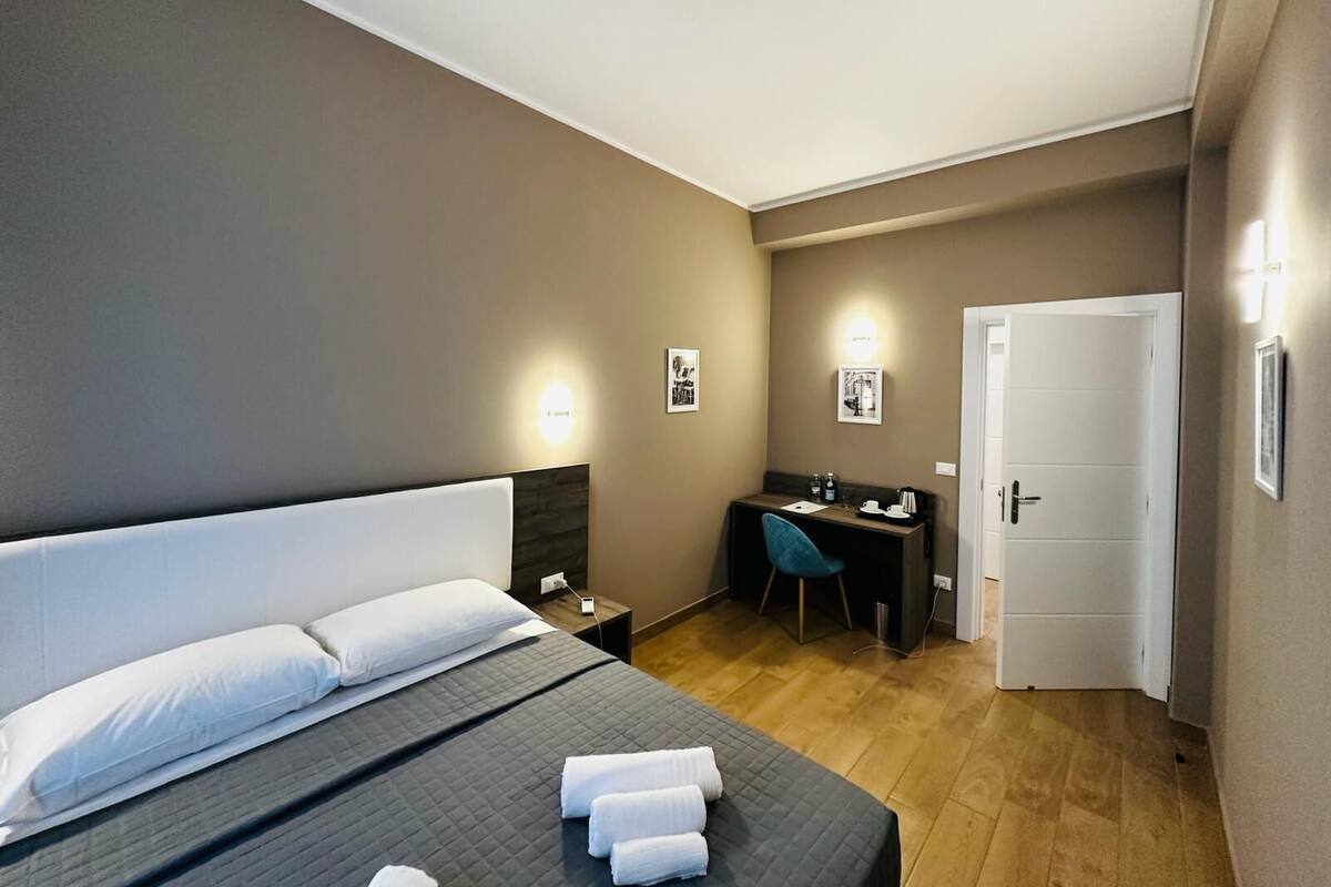 A hotel room with a bed, a desk, and a door.