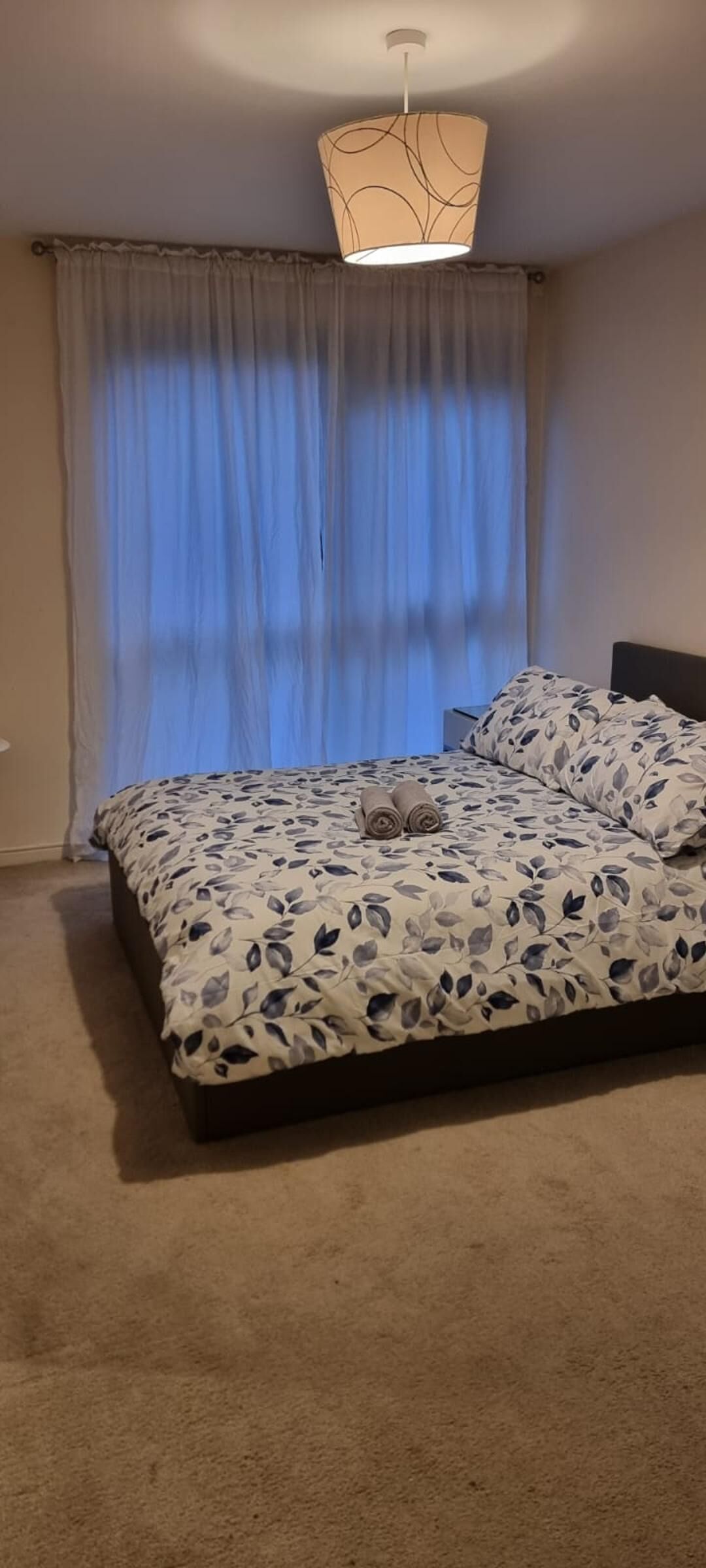 Un dormitorio con cama, luz de techo y ventana con cortinas.