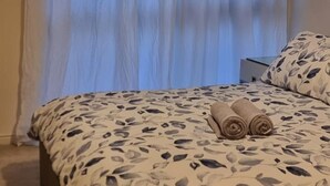 A bedroom with a bed, a nightstand, and a window with curtains. - Stunning 2-bed Apartment Near Colindale Station (London)