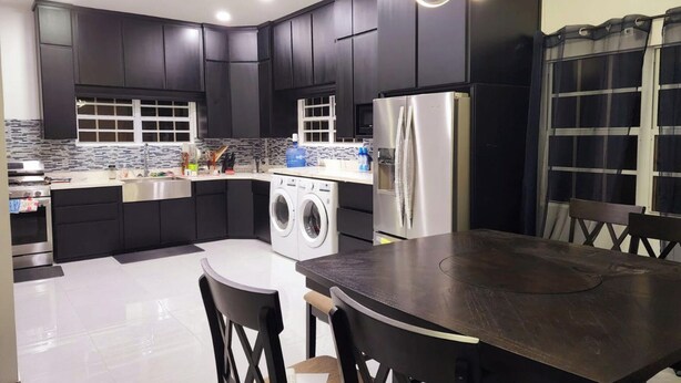 A modern kitchen with dark cabinets, a stainless steel refrigerator, a washing machine, and a dining area with a table and chairs. - Little Heaven - Remarkable Spot in Georgetown (Georgetown)